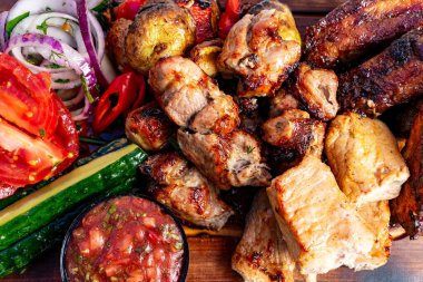 Domates, salatalık ve soğan gibi taze sebzelerin yanında tavuk ve domuz eti de dahil olmak üzere çeşitli ızgara etlerle dolu canlı bir tabak. Renkli ve iştah açıcı bir yemek sergileniyor..