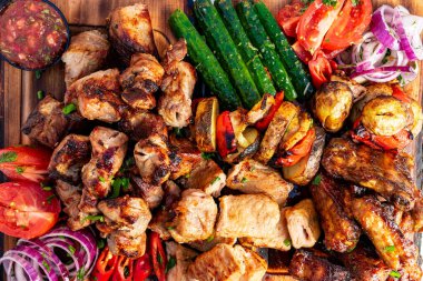 Ahşap bir tabakta canlı bir ızgara et ve sebze çeşidi sergilenir. Sulu tavuk kanatları ve şiş ete taze biber, soğan ve domates eşlik eder..