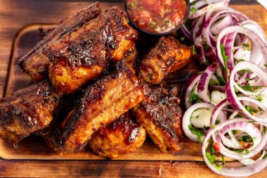 Dilimlenmiş soğan ve otlardan yapılmış canlı bir salatanın yanında, küçük bir kase taze salsa ile tamamlanmış, zengin bir sosla kaplanmış bir tabak yumuşak barbekü pirzolası duruyor..