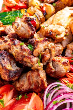 Canlı bir tabakta domates, soğan ve otlar gibi renkli taze sebzelerin yanında çeşitli ızgara etler yer alır. Bu yemek nefis bir açık hava yemeği sunuyor..