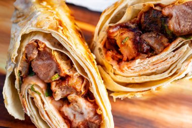 Izgara et ve baharatlı soslarla dolu taze yapılmış rulo köfteler ahşap bir tahtada sergileniyor. Canlı renkler ve günlük yemek ortamında dokular sergileniyor..