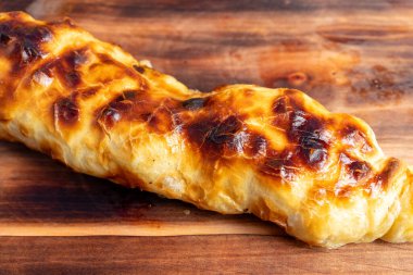 Çıtır çıtır çıtır pişmiş yeni pişmiş altın bir hamur işi ahşap bir yüzeyde duruyor. Süslü katmanları, duyularını baştan çıkaran, lezzetli bir dolgu olduğunu gösteriyor..