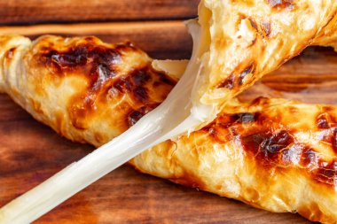 Erimiş peynirle dolu yumuşak hamur işleri kesilerek açılır ve yapışkan güzellikler ortaya çıkar. Altın-kahverengi kabuk kıtır kıtır, lezzetli ve lezzetli bir deneyimi davet ediyor..