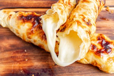 Tahta bir masanın üzerinde içi sıcak, yapışkan peynirle dolu lezzetli, taze pişmiş hamur işleri, altın gibi, çıtır çıtır bir dış görünüşü sergiliyor. Bu tatlar mükemmel bir doku ve lezzet karışımı sunuyor..