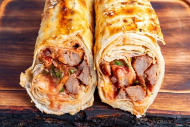 Tahta bir tahtanın üzerinde taze et ve sebzelerle dolu iki tane doyurucu paket sergileniyor. Kusursuzca kızartılmış, ambalajlar çıtır çıtır bir dış görünüşü gösteriyor, aromalı dolguyu ima ediyor..