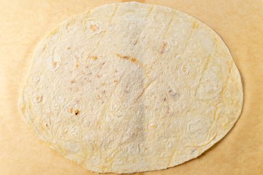 Sıcak bir mutfakta, taze bir tortilla düz bir yüzeye dayanır. Bu zımba yemek, sıcak rengi ve yumuşak dokusuyla lezzetli yemekler için hazır ev yapımı bir dokunuş sergiliyor..