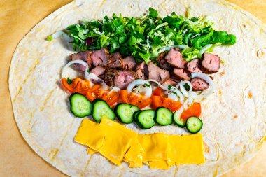 Fresh lettuce, onions, tomatoes, cucumbers, and cheese are layered on a tortilla with seasoned meat, ready to be rolled into a tasty wrap for a satisfying meal. clipart