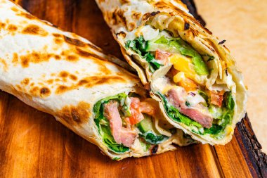 İki paket, canlı kıvrımlı marul, domates, peynir ve et sergileniyor. Köy ahşap bir tahtaya kurulurlar, taze renkleriyle iştahlarına davetiye çıkarırlar..