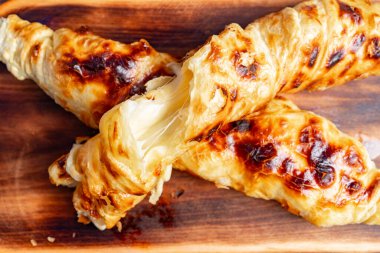 Taze pişmiş kruvasan tarzı hamur işleri, merkezden sızan erimiş peynirle birlikte taşralı ahşap bir tahtanın üzerinde duran altın, pullu bir dış görünüşü sergiliyor..