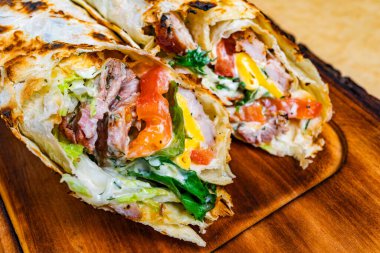 Ağız sulandıran burrito vitrinleri ızgara et, canlı sebzeler ve kremalı sos hepsi sıcak, kızarmış tortilla ile sade ahşap bir tahtanın üzerinde..