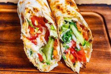 Lezzetli bir burrito rengarenk bir marul, domates, avokado ve peynir dokusunu ortaya çıkararak ikiye bölünür. Bu cezbedici yemek ahşap bir tabakta sunuluyor, taze malzemelerini sergiliyor..