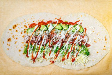 Izgara tavuk, taze sebze ve soslu canlı bir dürüm seriliyor. Hazırlıkta çeşitli renk ve dokular sergilenirken, sokak yiyecekleri seçeneği olarak cazibesine dikkat çekiliyor.