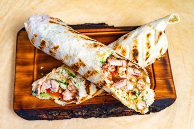 Ahşap bir tahtanın üzerinde ızgara tavuk, taze sebze ve lezzetli soslarla dolu taze yapılmış bir sargı duruyor. Bu iştah açıcı yemek sıradan bir öğle yemeği ya da akşam yemeği için mükemmel..