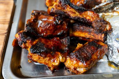 Lezzetli ızgara kaburgalar metal bir tepside üst üste yığılır ve zengin, karamelize bir jöle sergilenir. Açık hava, yaz toplantılarında mangal yapmak ve lezzet katmak için mükemmel olduğunu ima eder..