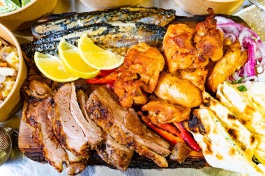 Renkli bir tabakta taze limon, biber ve soğanla süslenmiş tavuk ve balık da dahil olmak üzere çeşitli ızgara etler yer alıyor. Sağlıklı bir yemek için mükemmel..