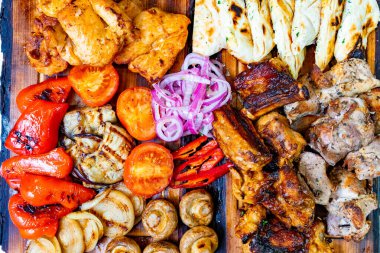 Lezzetli ızgara tavuk, tuzlu sosis ve taze sebzeler ahşap bir tabakta düzenlenir. Parlak domatesler, canlı biberler ve soğanlar bu doyurucu yemeğe renk katıyor..