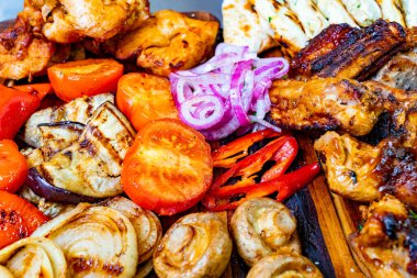 Ahşap tabakta bir dizi ızgara et, renkli sebzeler ve süslemeler sergileniyor..