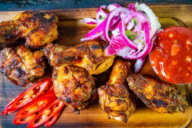 Sulu ızgara tavuk budu, canlı kırmızı soğanlar, taze acı biber dilimleri ve keskin bir sos eşliğinde ahşap bir tabakta düzenlenir. Tadını çıkarmaya hazır lezzetli bir yemek.