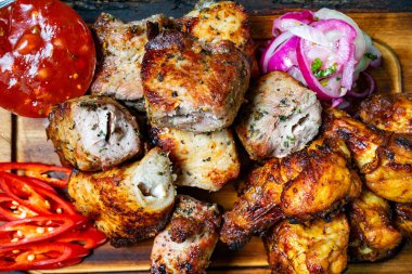 Ahşap bir tahtanın üzerinde leziz bir ızgara et çeşidi. Baharatlı sos, dilimlenmiş soğan ve kırmızı biberle birlikte. Festival sırasında paylaşmak için mükemmel..