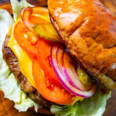 Lezzetli bir çizburger sulu bir biftek köftesi, erimiş çedar peyniri ve canlı domates, soğan ve turşu katmanları içerir, hepsi yumuşak, kızarmış bir çörek ve çıtır marul arasına yerleştirilir..