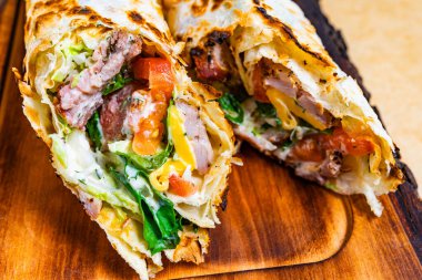 İki ızgara ambalaj malzemesi taze et, kıtır marul, domates ve peynir, hepsi zarif bir şekilde kızarmış tortilla ile sarılmış. Ahşap bir tahtada mükemmel servis ediliyor..