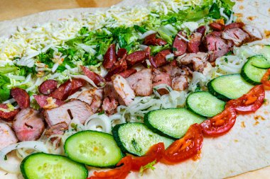 Canlı bir ambalajda ızgara et, marul, domates, salatalık ve peynir katmanları sergileniyor. Renkli malzemeler cazip bir yemek yaratıyor, öğle yemeği ya da atıştırmalık için mükemmel..