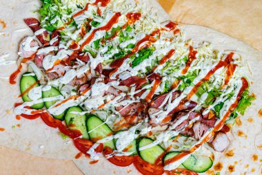 Renkli bir ambalaj kağıdı ızgara tavuk, kıtır marul, taze salatalık ve serpiştirilmiş soslar. Bu iştah açıcı yemek, tadını çıkarmaya hazır canlı malzemelerin altını çiziyor..