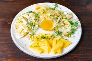 Taze yeşillikler ve küçük bir kase bal ile tamamlanmış yuvarlak bir tabakta zarif bir şekilde dizilmiş çeşitli peynirler. Bu mutfak vitrininde paylaşmak için bir davet aperatifi var..