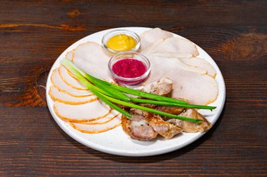 Mutfak vitrininde, canlı sosların yanında, kırsal ahşap bir masada dilimler halinde servis edilir. Taze yeşil soğanlar bu iştah açıcı düzenlemeye renk katar.