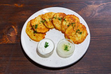 Bir tabak taze pişmiş patates gözlemesi, ekşi krema ve sosla birlikte otlarla süslenir. Bu yemek, yemek geleneklerini yansıtıyor..