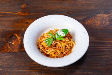 Bol et soslu, taze fesleğenle süslenmiş ve rendelenmiş bir tabak spagetti. Tabak ahşap bir masada oturuyor, doyurucu bir yemek deneyimini davet ediyor..