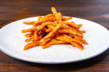 Terbiye edilmiş domuz kulağı yığını temiz beyaz bir tabağın üzerinde, zengin turuncu renklerini sergiliyor. Patatesler baharatla tatlandırılmış, onları cezbedici bir ziyafet yapıyor..