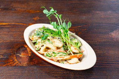 Karides, taze sebze ve mikroyeşilliklerin yer aldığı lezzetli bir salata kırsal ahşap bir masada sunuluyor. Canlı renkler onu çekici ve sağlıklı bir yemek seçeneği yapıyor..