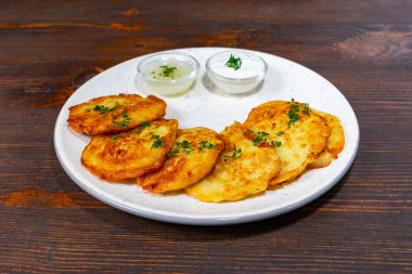 Taze otlarla süslenmiş bir tabak çıtır patatesli krep, iki küçük kase kremalı sos eşliğinde ahşap bir masada oturur. Paylaşmak ya da atıştırmak için mükemmel..