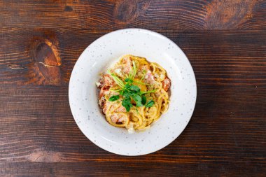 Köy ahşap bir masaya taze otlarla süslenmiş lezzetli bir tabak makarna konur. Yemek, yemek sevenlere cazip gelen kremalı bir sos içeriyor..