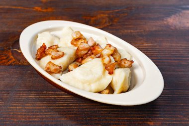 Çıtır pastırma parçalarıyla kaplı bir tabak taze hamur köftesi kırsal ahşap bir masaya konuyor ve lezzetli ve lezzetli bir konfor yemeği sergiliyor..