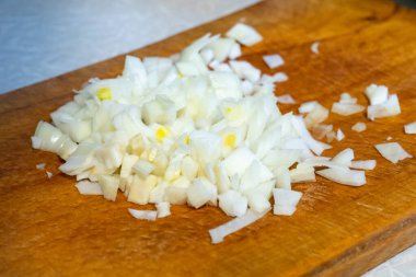 Modern bir mutfakta taze soğanlar ahşap bir kesme tahtasıyla ince ince doğranır. Çıtır çıtır beyaz parçalar lezzetli bir yemek hazırlığını sergiliyor..