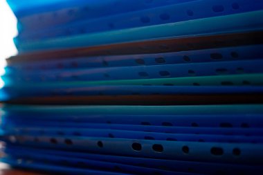 Mavinin çeşitli tonlarında canlı bir plastik klasör koleksiyonu düzgünce bir masanın üzerine istiflenmiştir. Işık renkleri yükseltir, organize ama dinamik bir çalışma alanı yaratır..