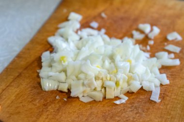 Taze doğranmış soğanlar ahşap bir kesme tahtasına saçılmış, pişirilmeye hazır. Mutfak çevresi yemek hazırlamak için sıcak ve davetkar bir ortam yaratıyor..