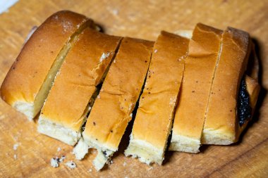 Bir somun haşhaş tohumu taze dilimlenmiş ahşap bir kesme tahtasıyla, içi yumuşak ve kabuklu dış görünüşünü sergiliyor. Sandviç ya da kızarmış atıştırmalık için mükemmel..