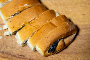 Bir somun tatlı haşhaşlı çörek dilimlenir ve zengin bir koyu dolgu ortaya çıkar. Ekmek ahşap bir yüzeye yerleştirilir, altın kabuğu ve davetkar dokusu sergilenir..