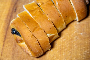 Yeni pişmiş haşhaşlı bir somun haşhaşlı çörek ahşap bir kesme tahtasının üzerinde düzgünce dilimlenmiş olarak oturur. Altın hamuru hafifçe çatlamış, yumuşak görünüyor.