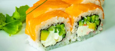 Canlı somon, kremalı avokado ve kıtır kıtır salatalıklı taze suşi ruloları. Yemek zarif bir şekilde wasabi ile kaplanmış ve lezzetli bir sunum için yeşilliklerle süslenmiş..