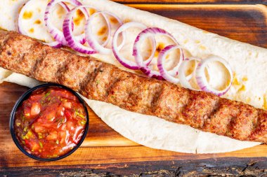 Izgara kebap taze kırmızı soğan dilimleriyle süslenmiş sıcak bir ekmeğin üzerinde oturur. Canlı bir salsa sosu tabağı tamamlar ve çekici bir yemek oluşturur..