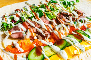 Canlı ambalajlar rengarenk malzemeler sunar. Izgara et, taze marul, domates, salatalık ve kremalı soslar. Hepsi büyük bir tortilla üzerinde güzelce yerleştirilmiş..