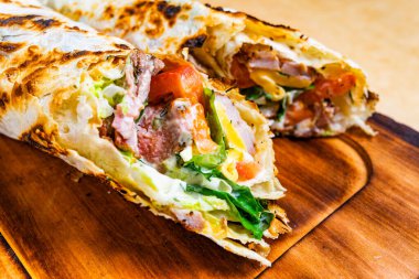 Ahşap bir tahtanın üzerinde lezzetli bir paket var. Taze sebzeler, domatesler ve ızgara etler sergileniyor. Kızarmış tortilla çekici bir aroma yayar, tatmin edici bir yemek davet eder..