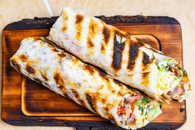 İki taze ızgara burrito ahşap bir tahtanın üzerinde, içi taze et, taze marul ve olgun domateslerle dolu. Dürümler çıtır çıtır, yanmış bir dış görünüş sergiliyor..