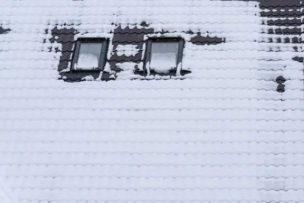 Taze bir kar tabakası iki pencereli bir çatı örtüsü. Sakin kış manzarası, kar tanelerinin yavaşça düşmeye devam ettiği sakin bir atmosfer yaratıyor..