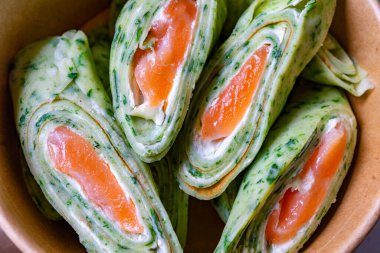 Somon dilimleriyle dolu rulo ıspanak paketleri bir kasede sunulur. Canlı yeşil, pembemsi balıkları vurgular, iştah açıcı ve sağlıklı bir yemek oluşturur..