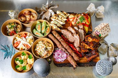 Çeşitli yemeklerden oluşan şenlikli bir düzenleme ızgara et, salata ve aperatifleri içeriyor. Hepsi de ahşap bir tabakta güzelce sunuluyor..